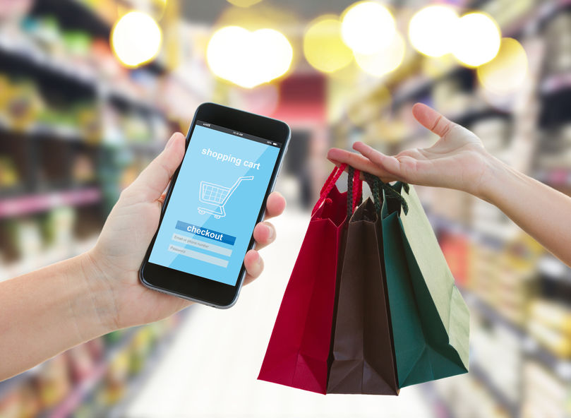 hand holding mobile smart phone with mobile shop on supermarket blur background and shopping bags - e-commerce concept