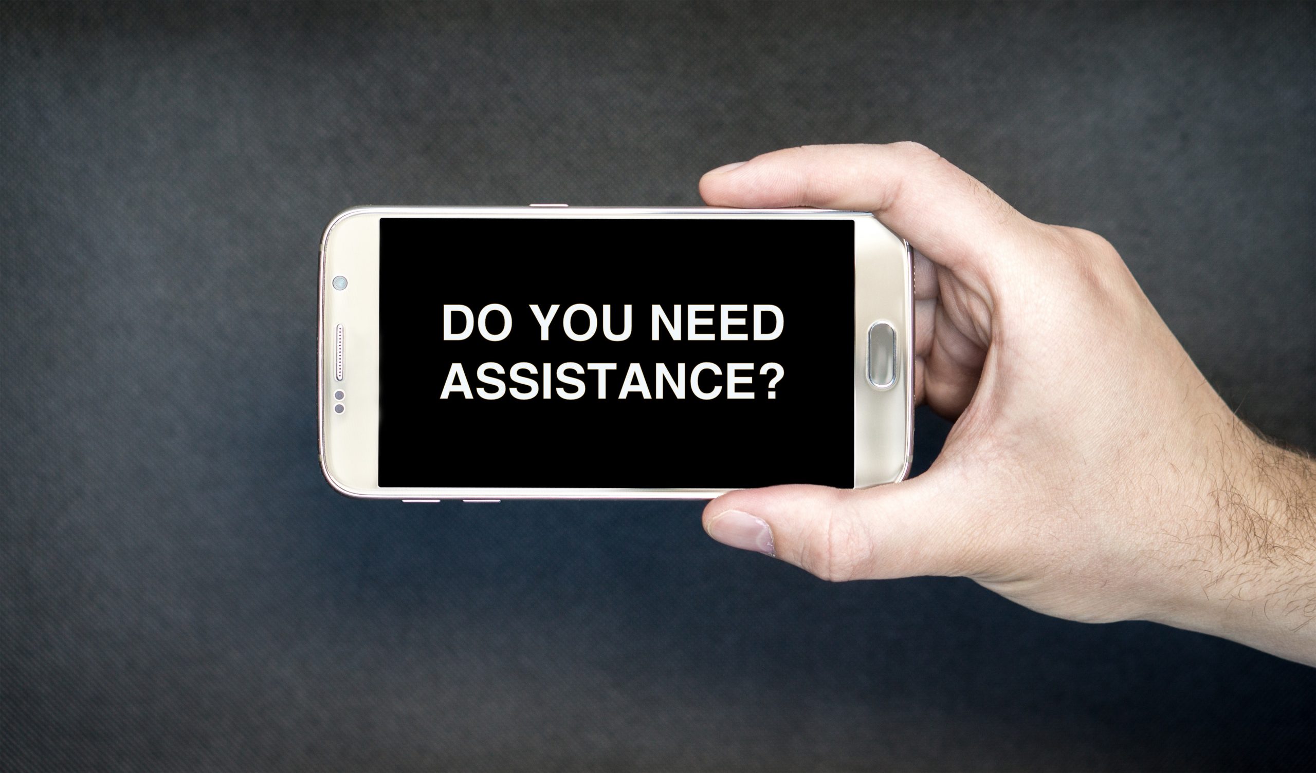 Hand holding a cell phone with the message Do You Need Assistance?